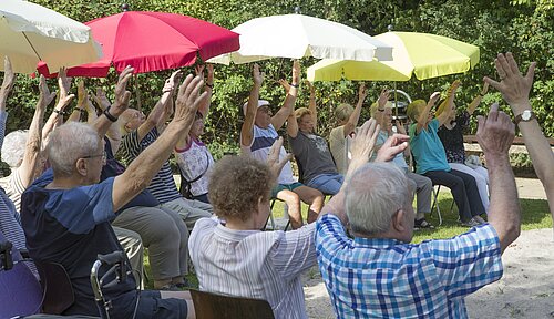 Bewohnergruppe in Rollstühlen bei morgentlicher Gymnastik im Park