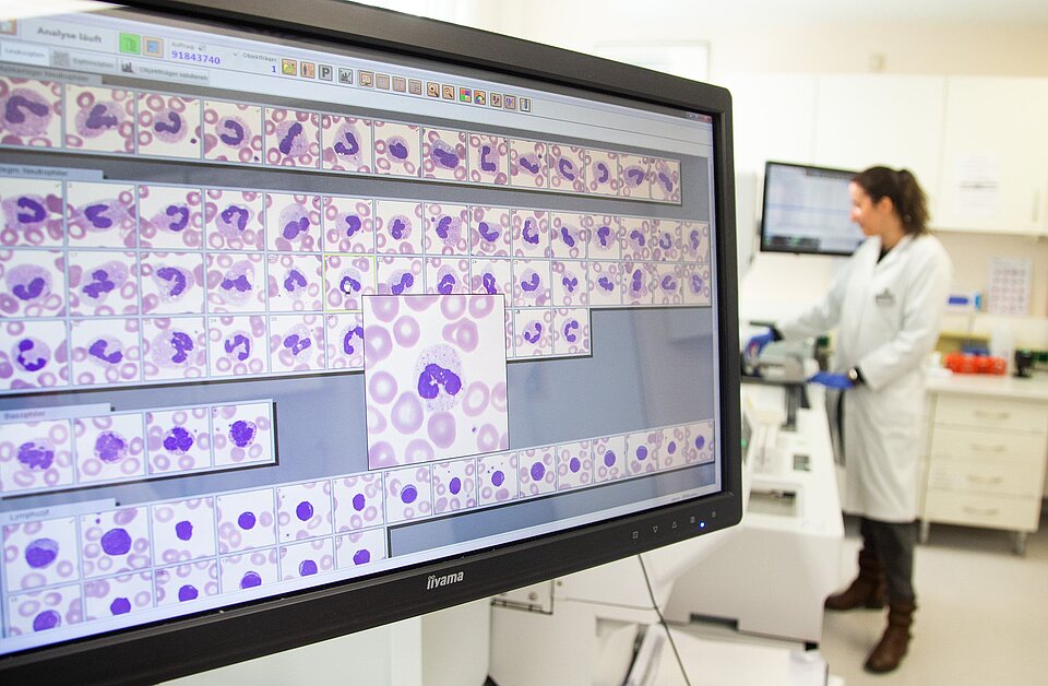 Laborergebnisse auf Monitor und Mitarbeiterin im Hintergrund